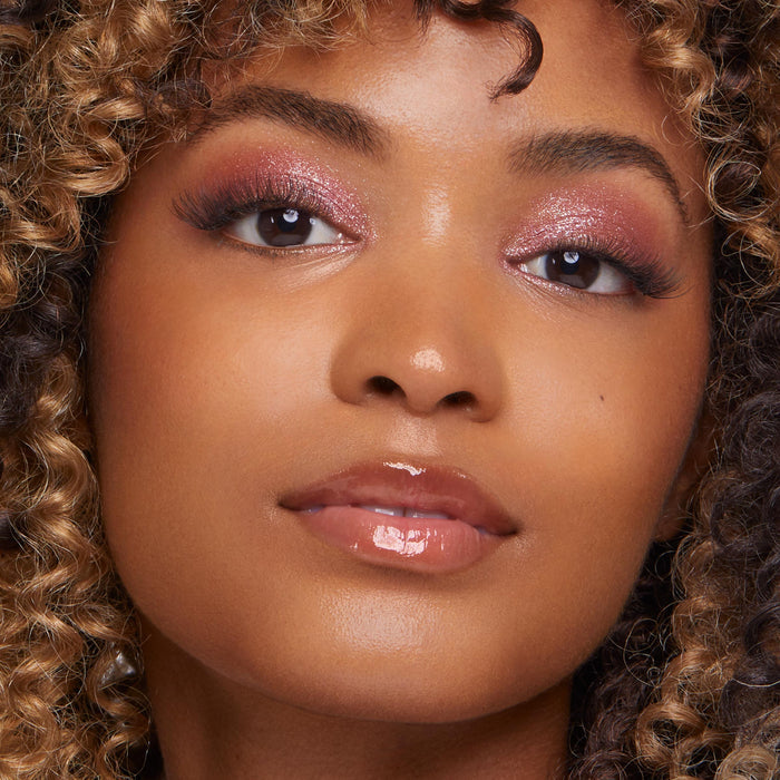 Model wears ColourPop Party of Five Super Shock Shadow, a shimmery rose-pink eyeshadow on the lids with soft blend and sparkle, shown in a close-up with wispy lashes, dewy skin, and glossy nude lips.