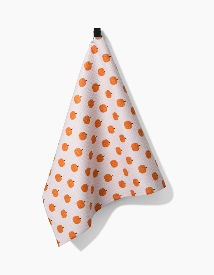 White towel with pumpkin pattern hanging on a black hook against a white background