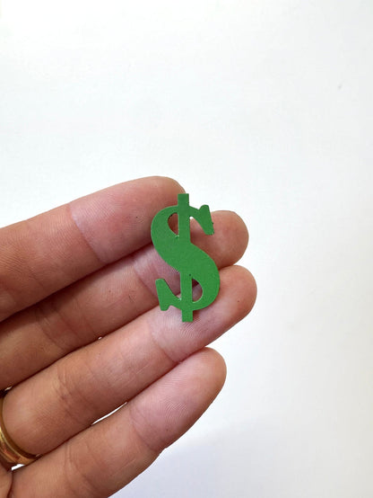 A small green dollar sign magnet  held between a person's fingers against a plain white background.