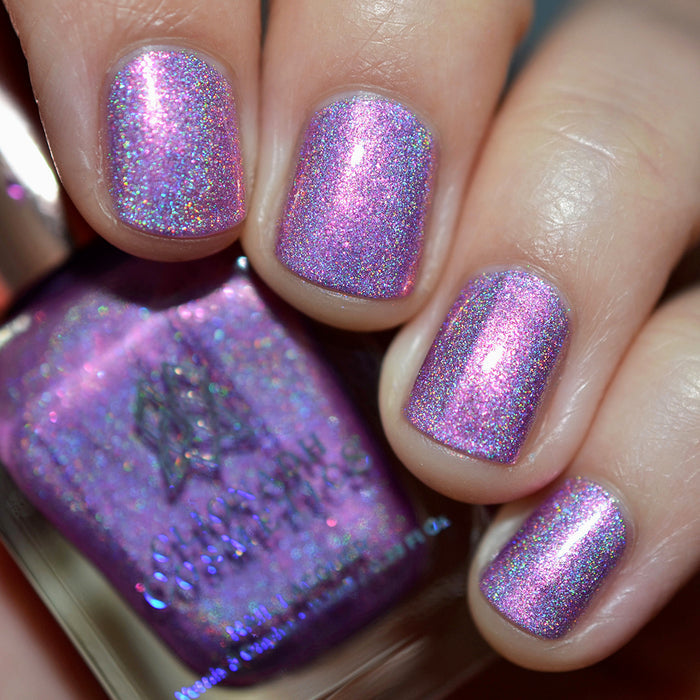 Close-up of nails painted with P.B. & Holo Nail Lacquer on fair skin tone. Hand is holding polish bottle.