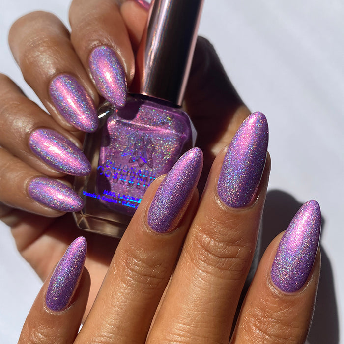 Close-up of nails painted with P.B. & Holo Nail Lacquer on medium skin tone. Hand is holding polish bottle.