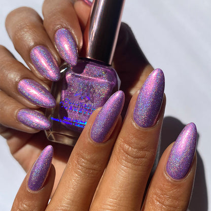 Close-up of nails painted with P.B. & Holo Nail Lacquer on medium skin tone. Hand is holding polish bottle.