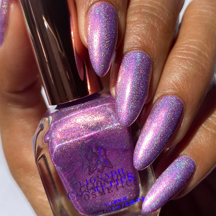 Close-up of nails painted with P.B. & Holo Nail Lacquer on medium skin tone. Hand is holding polish bottle.