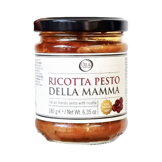 A jar of Pesto della Mamma Ricotta, showing a clear glass jar with the pesto inside and a black lid. The label includes the product name and a brief description.