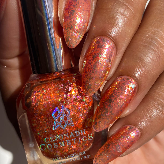 Close-up of nails painted with Autumn Acres Nail Lacquer on medium skin tone. Hand is holding polish bottle.