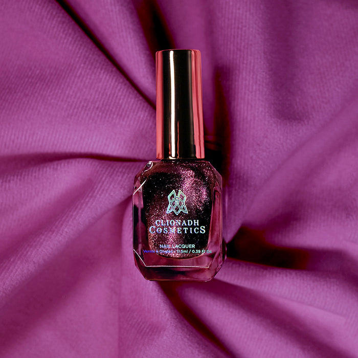 Bottle of nail polish containing Plush Pink on a purple fabric background.