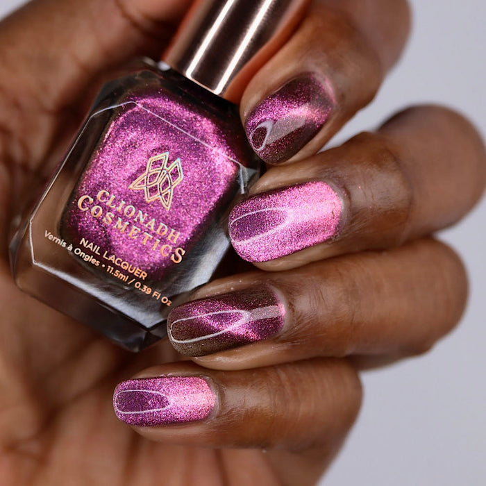 Close-up of nails painted with Plush Pink Nail Lacquer on deep skin tone. Hand is holding polish bottle.