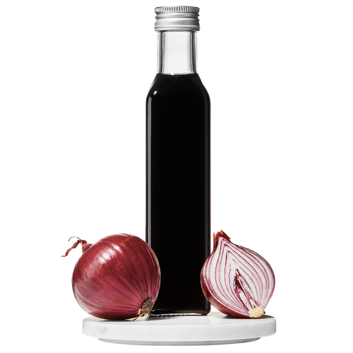 A clear glass bottle of Red Onion Balsamic Vinegar with a cap on top. A whole red onion and a slice of red onion are placed beside the bottle.