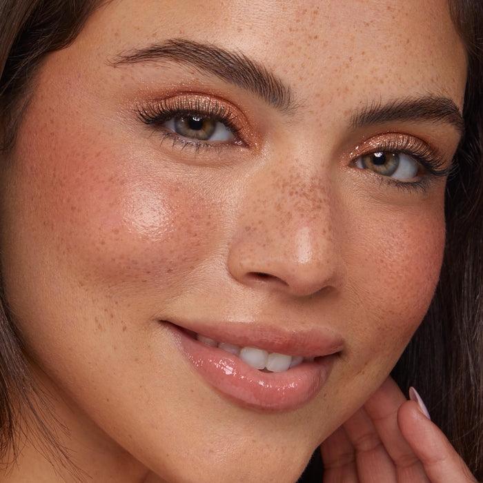 Shimmery lids showcase ColourPop Super Shock Shadow Ritz, a sparkly champagne wash catching light on the upper lids; close-up of a smiling model with freckles, peachy blush, and glossy nude lips for soft everyday glam.