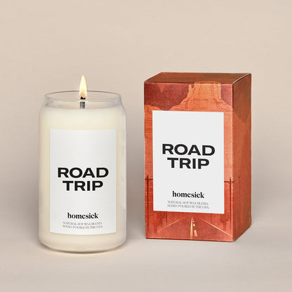A lit Roadtrip candle sitting next to the a graphic packaging box.
