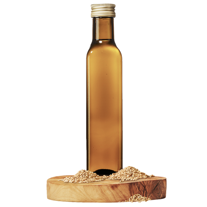 A bottle of roasted sesame oil placed on a wooden stand with sesame seeds scattered around.