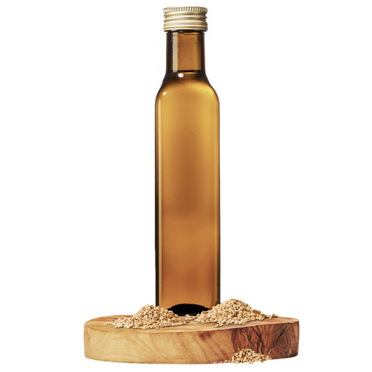 A bottle of roasted sesame oil placed on a wooden stand with sesame seeds scattered around.
