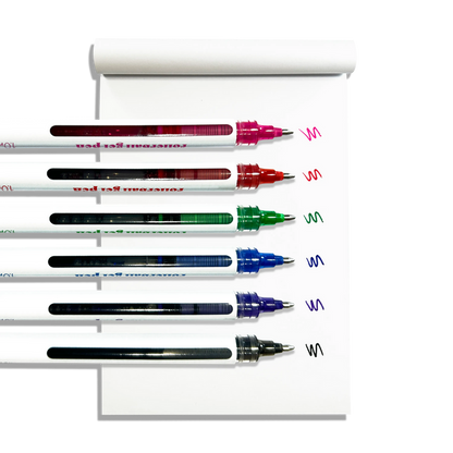 Row of uncapped OOLY Seriously Smooth Rollerball Gel Pens with color swatches on a white notepad on a white background