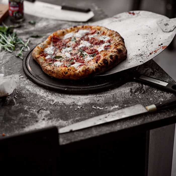 This is an image of baked pizza being transferred from a Breeo Pizza Peel to a Breeo Serving Board