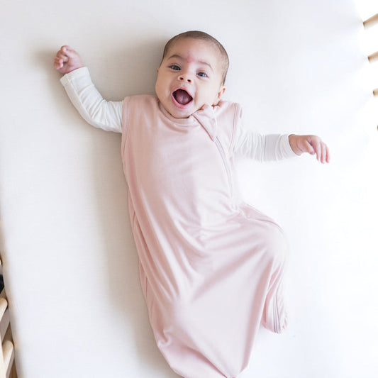 Smiling baby wearing the 0.5 Tog Sleep Bag in Blush with a Cloud long sleeve romper underneath