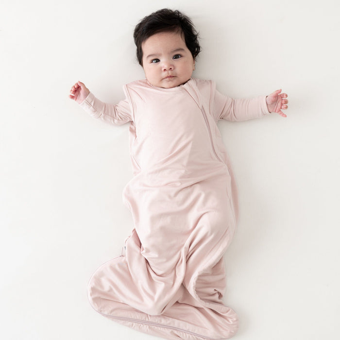 Baby laying on white surface while wearing Kyte Baby Sleep Bag in Blush TOG 0.5