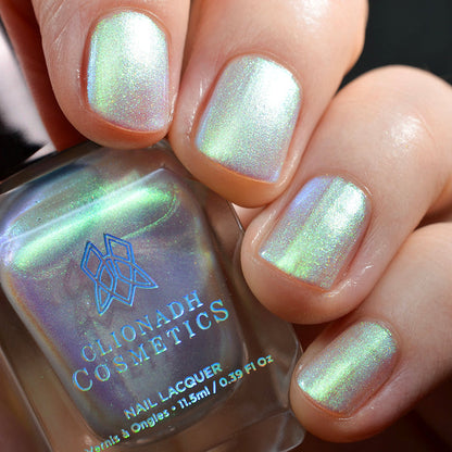 Close-up of nails painted with Lucidum Nail Lacquer on fair skin tone. Hand is holding polish bottle.