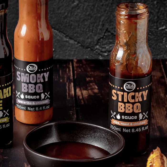 two jars of sauces made for barbecuing Sticky BBQ sauce and Smoky BBQ sauce both on a wooden board with a small dish of sauce in the foreground
