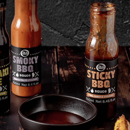 two jars of sauces made for barbecuing Sticky BBQ sauce and Smoky BBQ sauce both on a wooden board with a small dish of sauce in the foreground