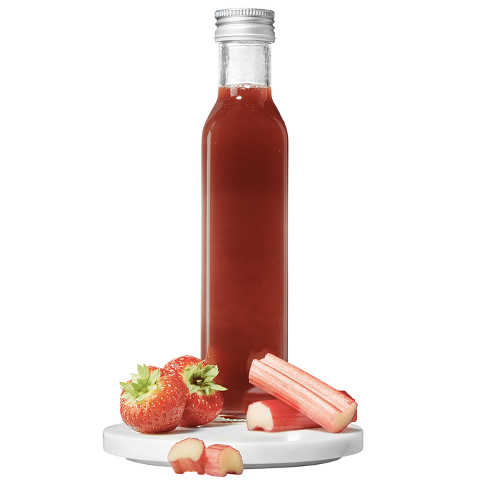 A clear bottle containing red strawberry rhubarb pulp vinegar, with a silver cap, accompanied by fresh strawberries and rhubarb pieces to the side.