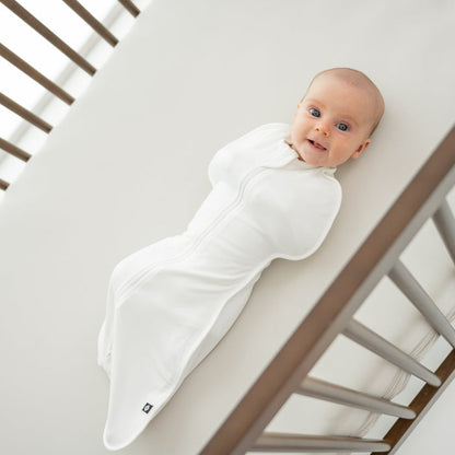 Baby in a wooden crib wearing a white swaddle bag