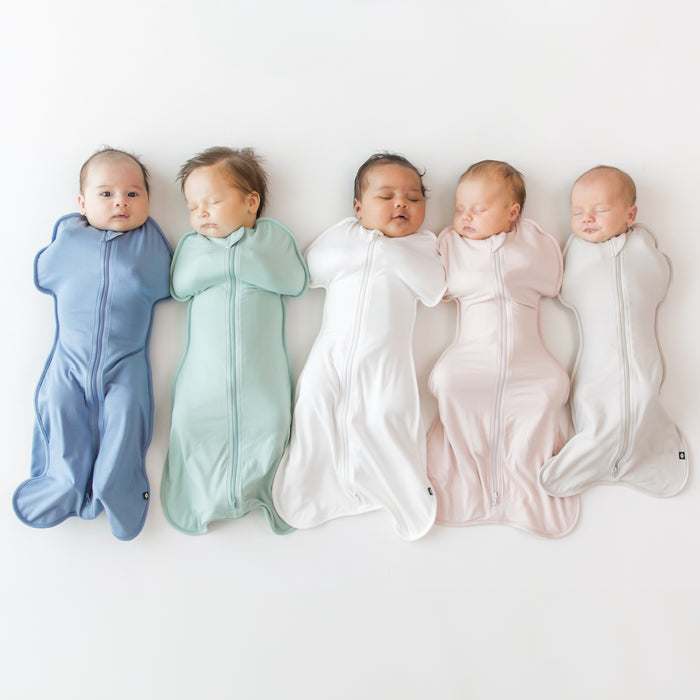 Group of 5 babies in Kyte Baby Swaddle Bags in colors slate, sage, cloud, blush and oat