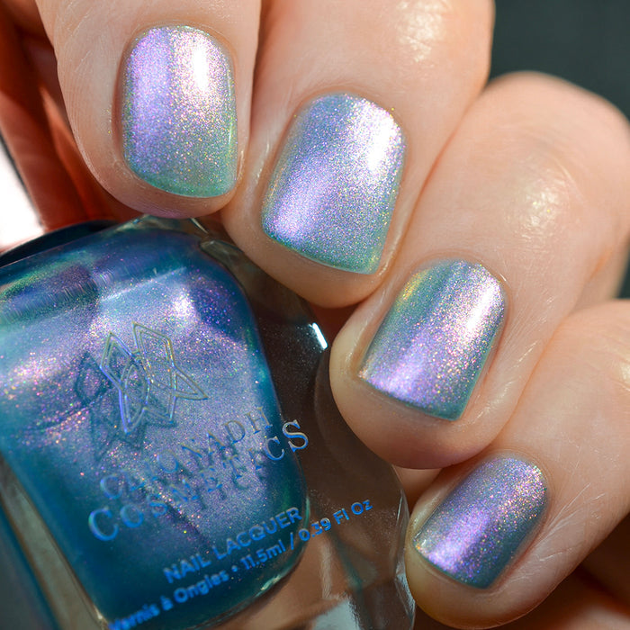 Close-up of nails painted with Tessera Nail Lacquer on fair skin tone. Hand is holding polish bottle.