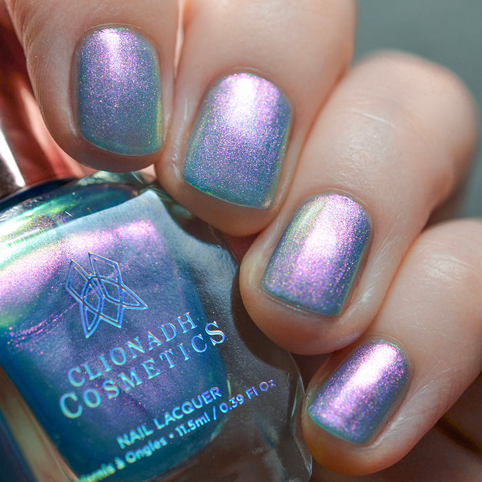 Close-up of nails painted with Tessera Nail Lacquer on fair skin tone. Hand is holding polish bottle.