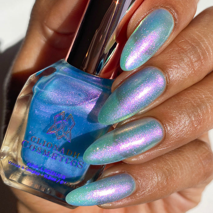 Close-up of nails painted with Tessera Nail Lacquer on medium skin tone. Hand is holding polish bottle.