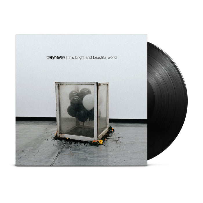 A classic black vinyl peeks out of a light gray jacket that shows a dirty box of mostly black and one white balloon inside. Around the box is some dirt and yellow flowers surrounding it on the floor.