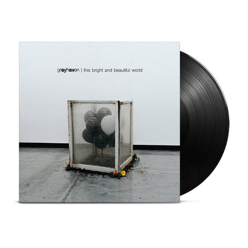 A classic black vinyl peeks out of a light gray jacket that shows a dirty box of mostly black and one white balloon inside. Around the box is some dirt and yellow flowers surrounding it on the floor.