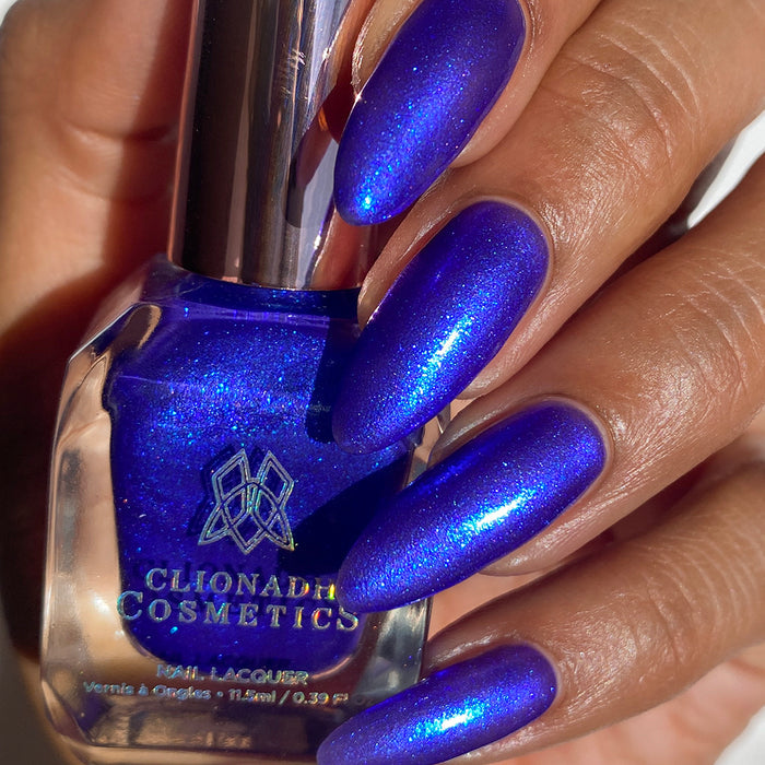 Close-up of nails painted with Tiara Nail Lacquer on medium skin tone. Hand is holding polish bottle.