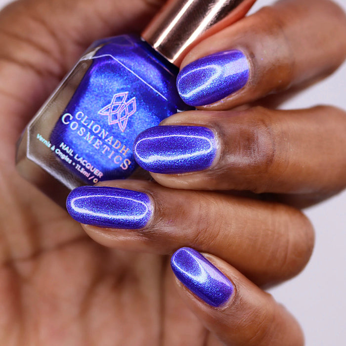 Close-up of nails painted with Tiara Nail Lacquer on deep skin tone. Hand is holding polish bottle.