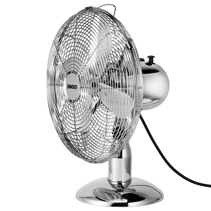 Der Unold TISCHVENTILATOR CHROME ist ein metallisch glänzender Tischventilator mit rundem Standfuß, Schutzgitter, sichtbaren Flügeln und einem schwarzen Netzkabel, das auf der Rückseite herausragt.