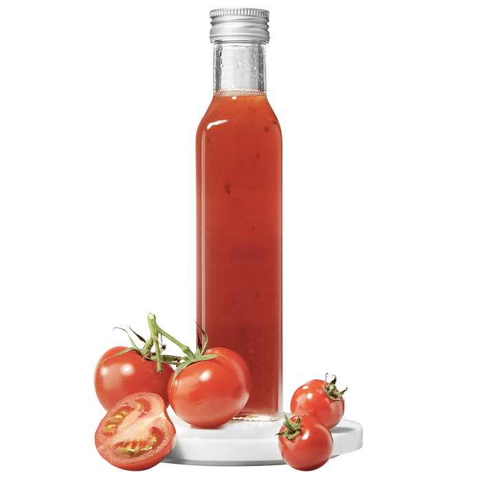 A tall, slender bottle of tomato pulp vinegar, with fresh tomatoes displayed in front.
