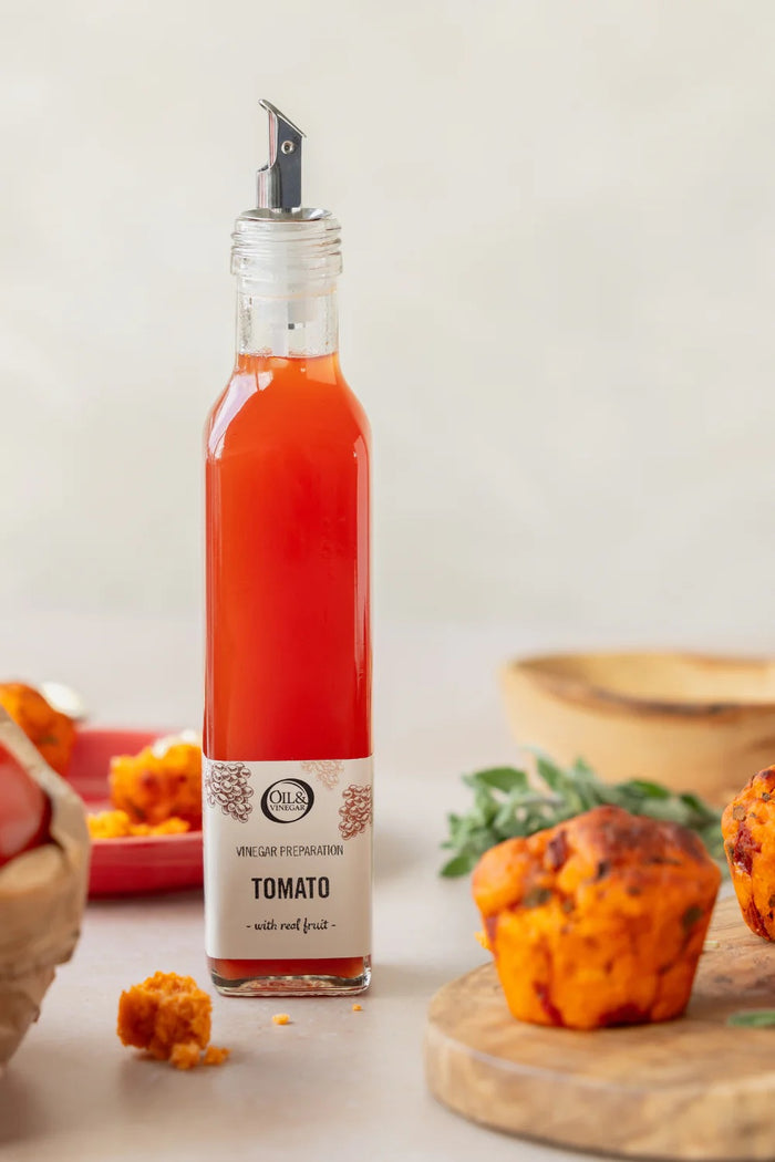 Bottle of tomato vinegar with a label on a table with muffins and ingredients.