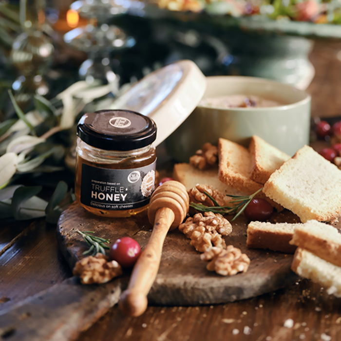 Jar of truffle honey on a board with crackers, walnuts, cranberries, and rosemary.