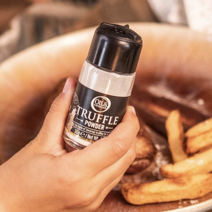 A hand holding a jar of truffle powder with a black lid with potatoes in the background