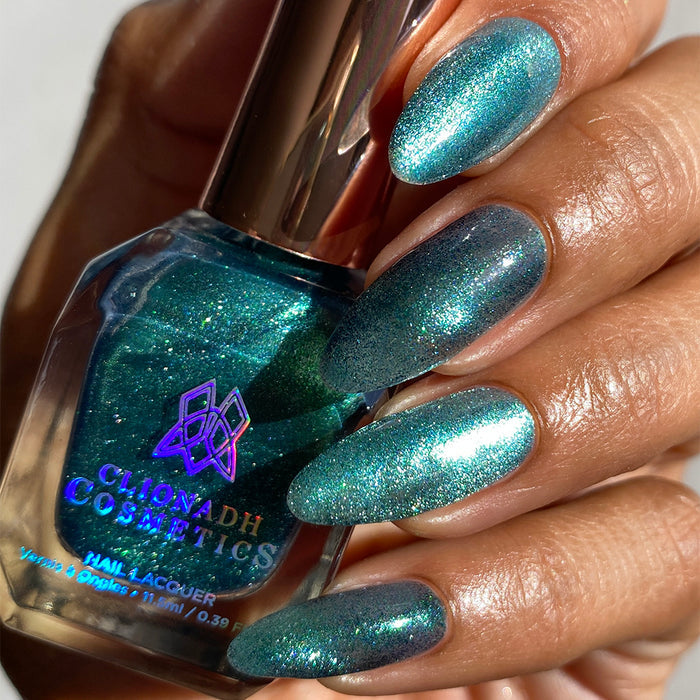 Close-up of nails painted with Turquoise Silk Nail Lacquer on medium skin tone. Hand is holding polish bottle.