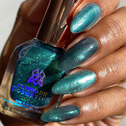 Close-up of nails painted with Turquoise Silk Nail Lacquer on medium skin tone. Hand is holding polish bottle.