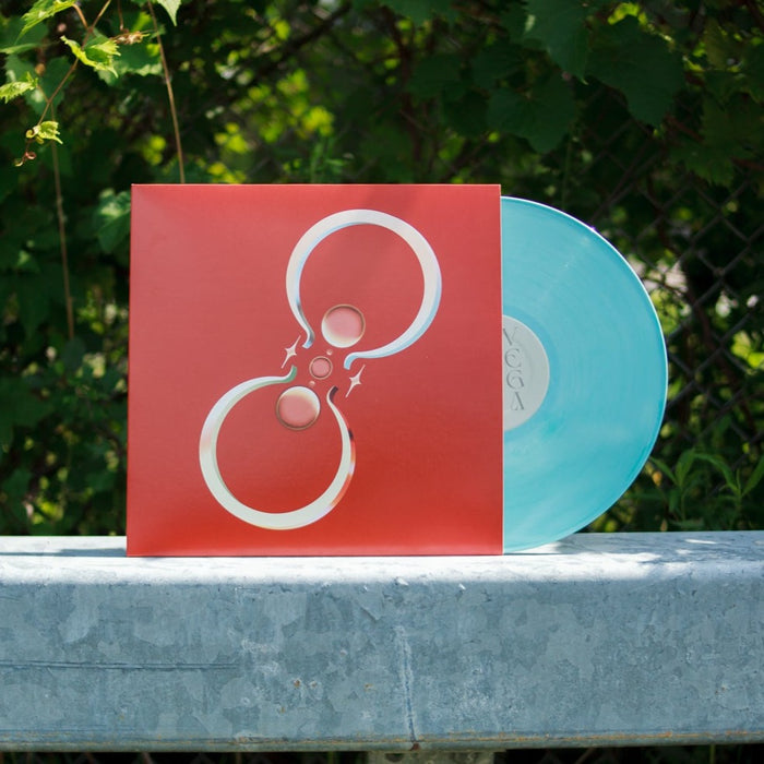 An Anberlin baby blue LP vinyl, partially in its red sleeve with a white abstract design, is set outdoors on concrete with leafy green plants in the background.