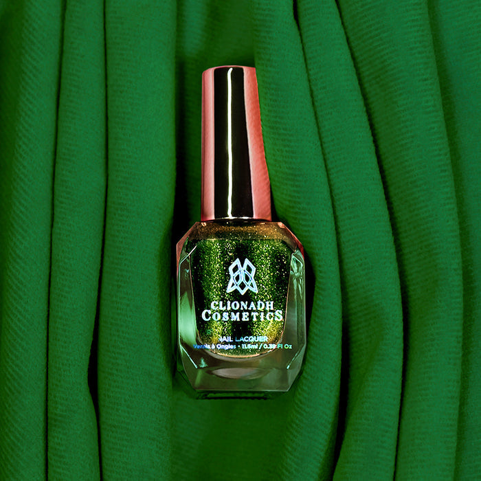 Bottle of nail polish containing Velvet Verdigris on a green fabric background.