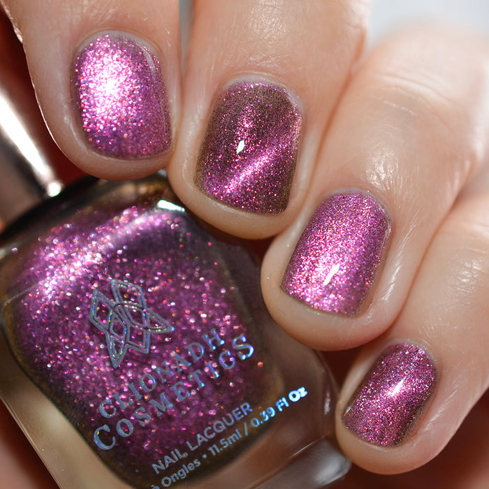 Close-up of nails painted with Plush Pink Nail Lacquer on fair skin tone. Hand is holding polish bottle.