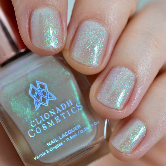 Close-up of nails painted with Venus Nail Lacquer on fair skin tone. hand is holding polish bottle.