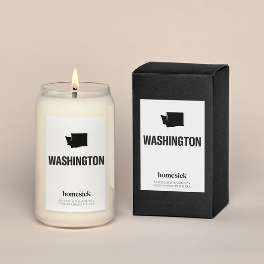 A lit Washington Homesick candle displayed next to its boxed packaging on a dark cream background.