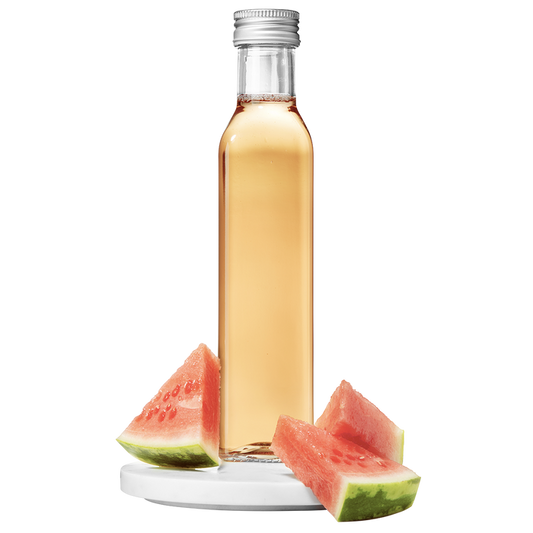 A clear bottle of watermelon vinegar with a silver cap, accompanied by slices of fresh watermelon.