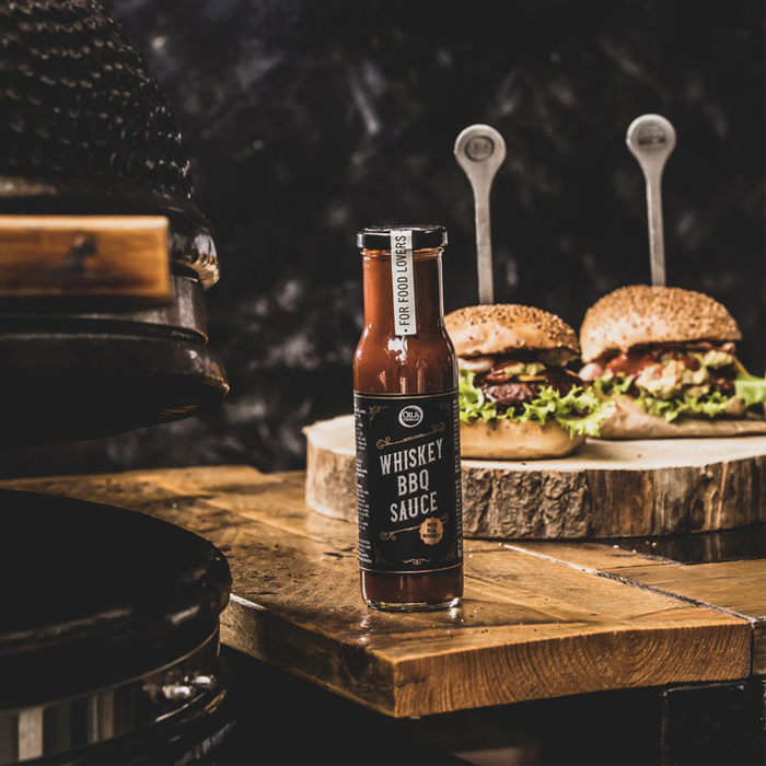A bottle of Whiskey BBQ sauce on a wooden table with two gourmet burgers