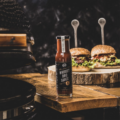 A bottle of Whiskey BBQ sauce on a wooden table with two gourmet burgers