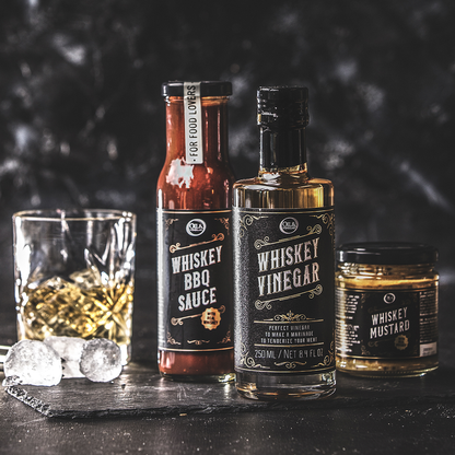 A bottle of whiskey bbq sauce on a black table next to a Whiskey vinegar and Whiskey mustard