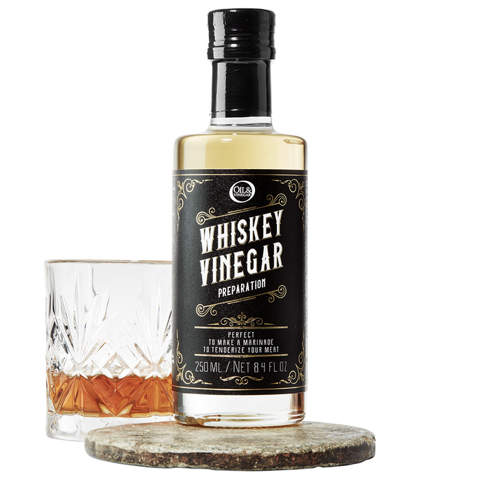 A bottle of whiskey vinegar with a label that reads 'WHISKEY VINEGAR', accompanied by a glass filled with a amber-colored liquid.